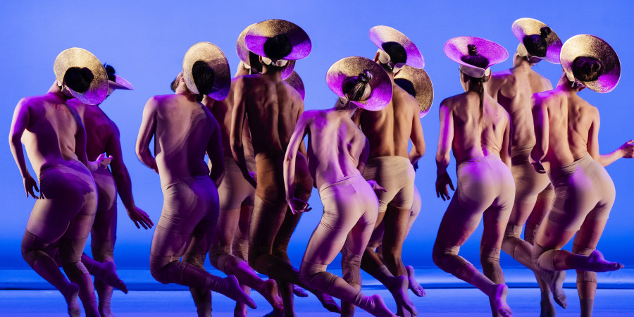 Eine Gruppe von Frauen tanzt mit dem nackten R&uuml;cken zum Publikum mit violetten Kopfbedeckungen